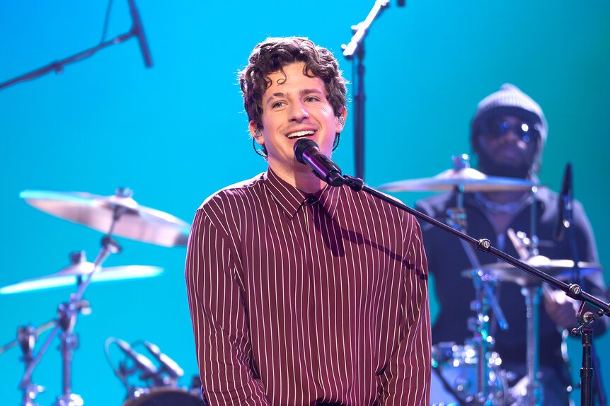 Charlie Puth on stage with microphone and band during a concert.